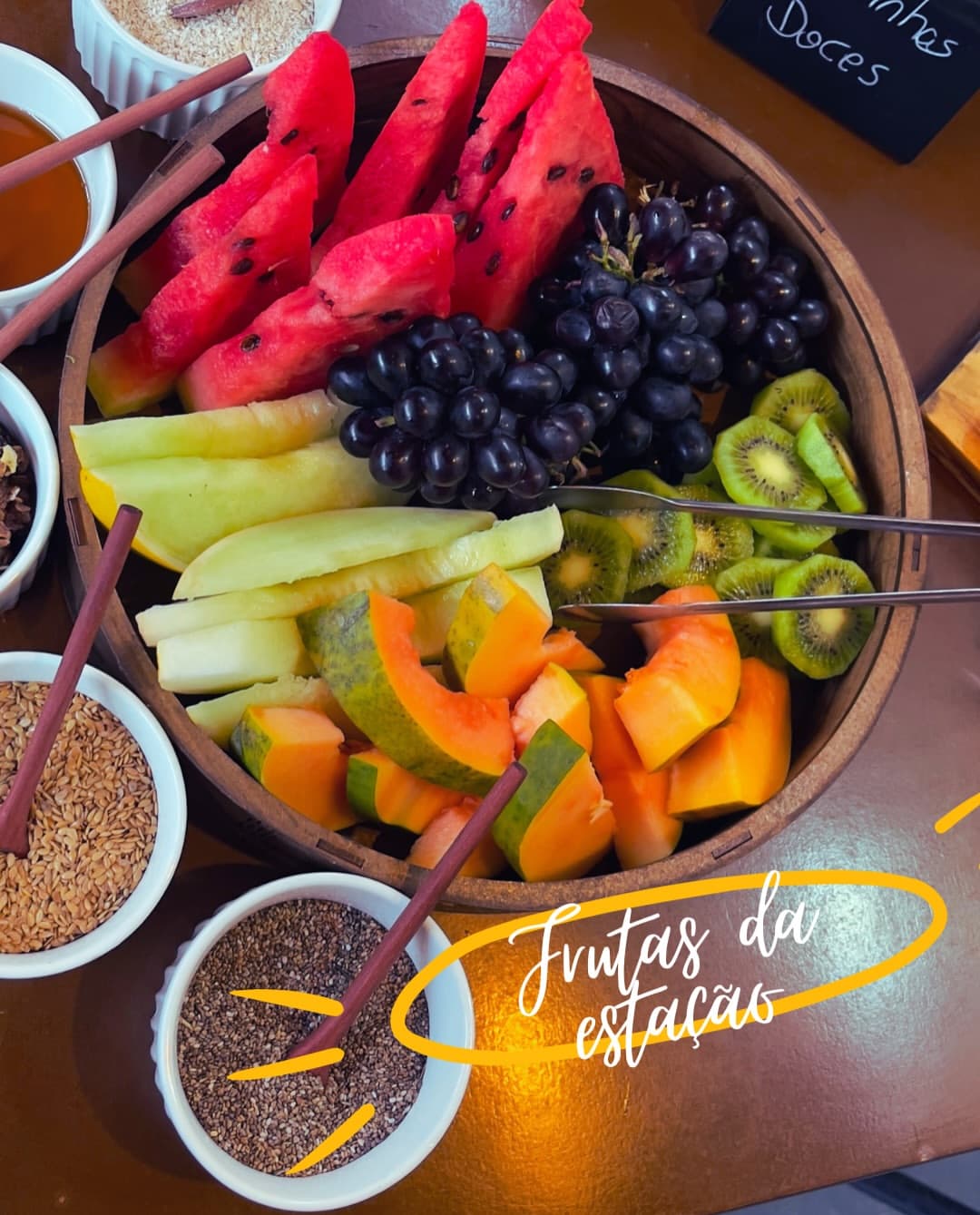 Café colonial: frutas da estação — melancia, uva, kiwi, mamão e melão — com mel e sementes.