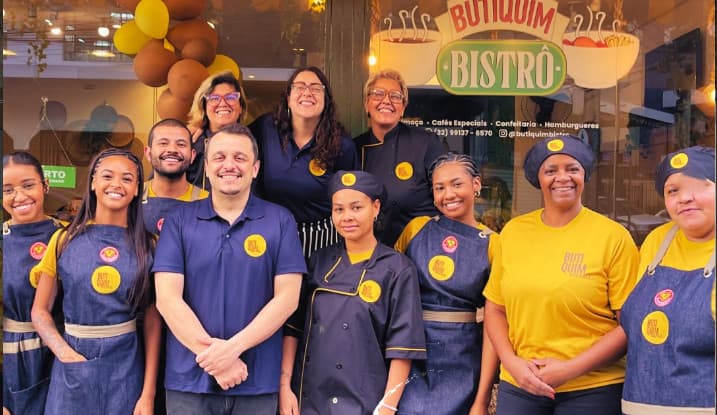 Equipe do Butiquim Bistrô reunida em frente à loja, com uniformes azuis e camisetas amarelas.