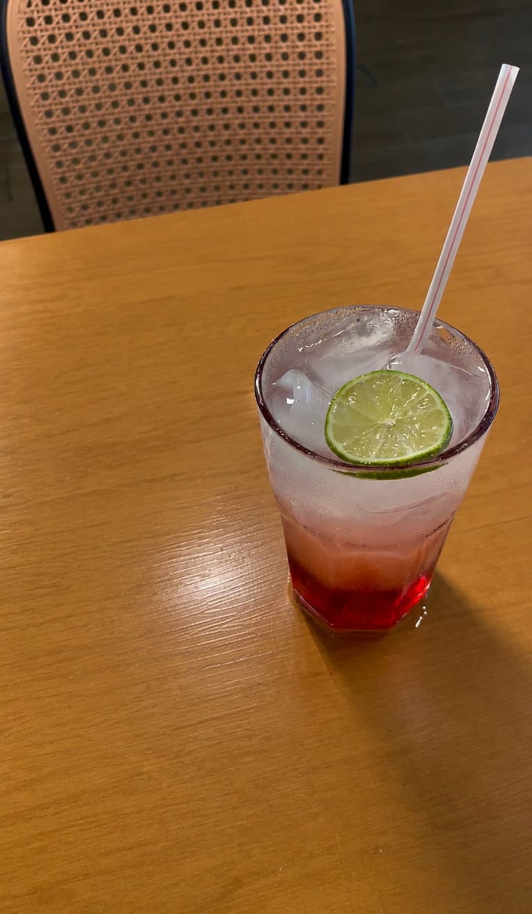 Soda italiana em copo alto com gelo e rodela de limão, em mesa de madeira.